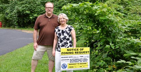 Gene and Margaret Middleton stand behind the City of Blue Ridge’s Notice of Zoning Request sign, located before the potential townhome and designer cottage community, which is just feet from their residence.