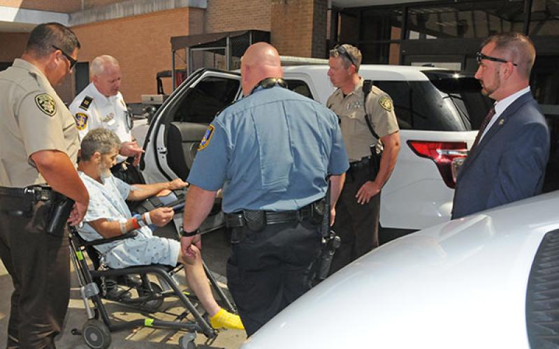 Law enforcement officers prepare to put James Larry Parris Jr., (in chair) into a McCaysville patrol vehicle outside WellStar Kennestone Hospital in Marietta last Thursday at noon. McCaysville officers shown are, Det. Capt. Billy Brackett, second from left; McCaysville Patrolman Mark Chastain, with back to camera; and McCaysville Police Chief Michael Earley, right.