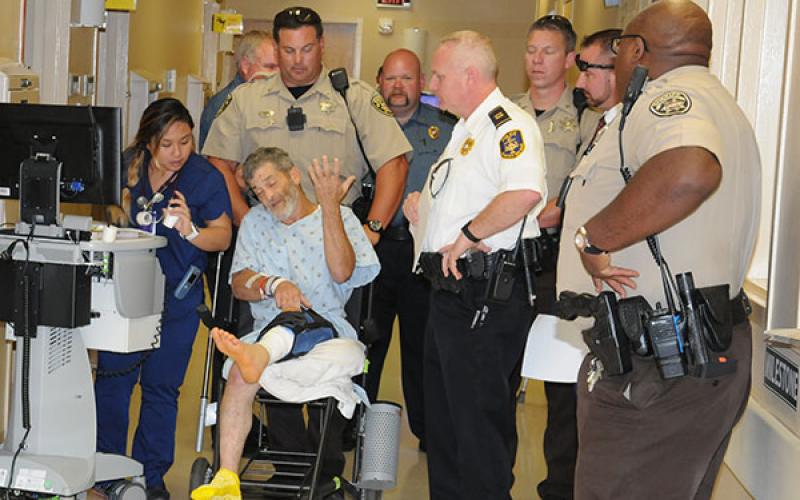 Deputies from the Cobb County Sheriff’s Office served warrants on James Larry Parris Jr., (in chair) before turning him over to McCaysville police officers shortly before noon Thursday. Shown with the Cobb County deputies as Parris is taken from WellStar Kennestone Hospital are McCaysville Patrolman Pete Kusek (in background), McCaysville Patrolman Mark Chastain, McCaysville Det. Capt. Billy Brackett, and McCaysville Police Chief Michael Earley.Law enforcement officers prepare to put James Larry Parris Jr.,