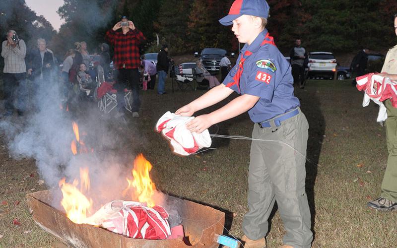 Eian Holloway, a Cub Scout with Pack 432, throws a tattered flag into the fire during the Flag Retirement ceremony at Ron Henry Horseshoe Bend Park Tuesday, October 22.