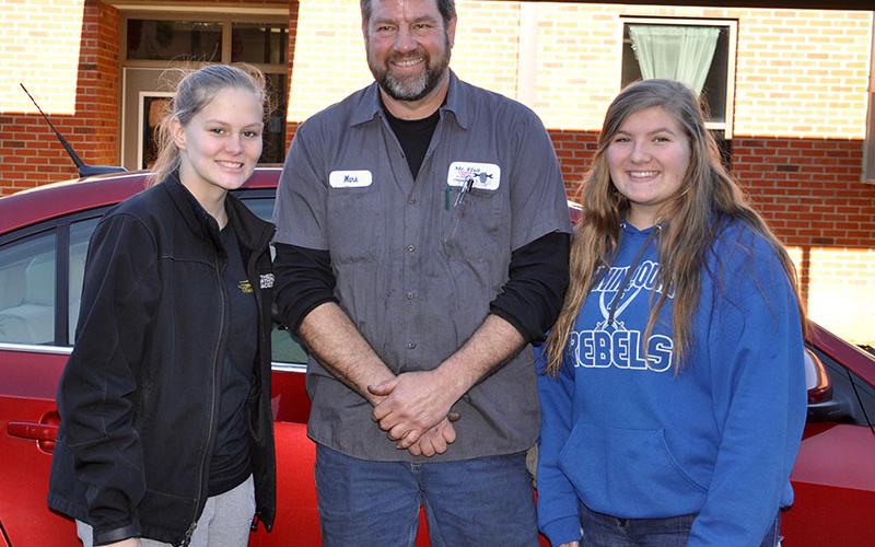 Fannin County High School (FCHS) student Alexis Hill, left, Mechanic Mark Keaton and FCHS student Bailey Pettit smile after learning to change a tire, check a tire’s air pressure and check a car’s oil Thursday, December 5.