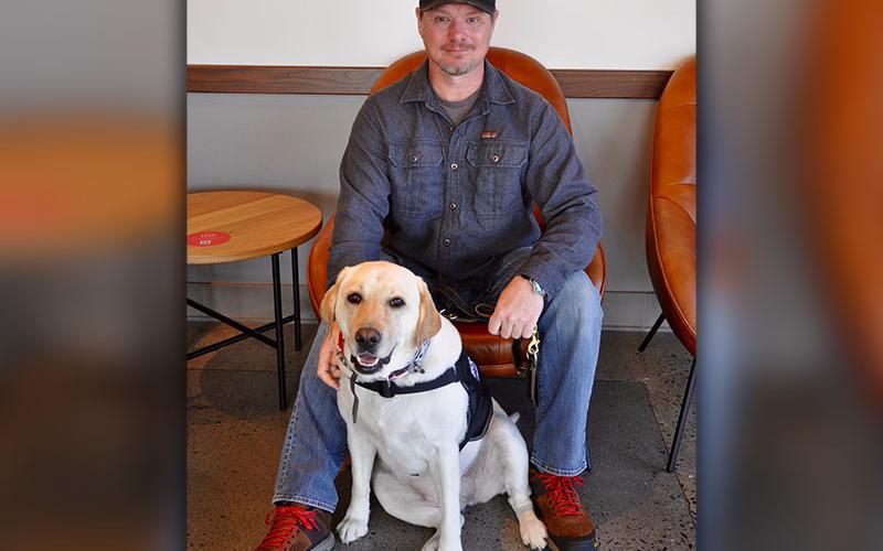 Retired U.S. Army Staff Sergent Stephen Fry Jr., sits with service dog Valor at one of his Operation Supply Drop Afghanistan checkpoints, Starbucks of Blue Ridge.