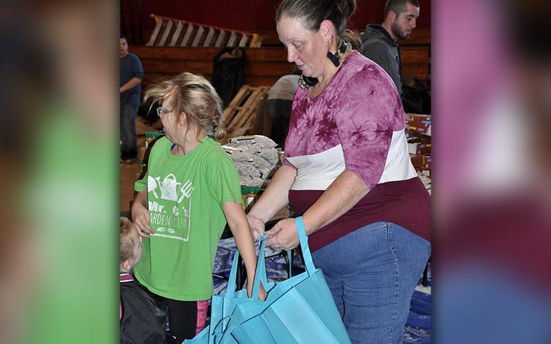 Volunteer Carrie Beaver holds reusable bags while a young volunteer fills them with peanut butter and tomato sauce.