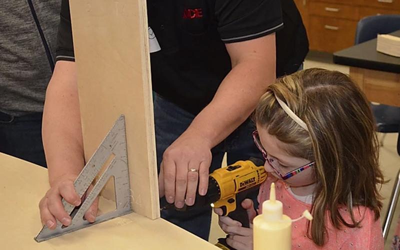 A student uses a drill with the help of a volunteer as they constructed a soap box derby car. The event re-enforces STEM lessons taught in school and also acts as a fundraiser for schools.