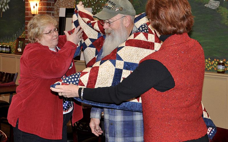 Susan Young with the Quilts of Valor Foundation, left, and quilter Robin Czyscon present U.S. Army veteran Chuck Bowen III with his own unique quilt Wednesday, January 29.