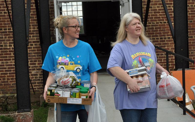Amanda Pittman, left and Jill Crago Rose carry food and supplies to vehicles during the March 19 food distribution.