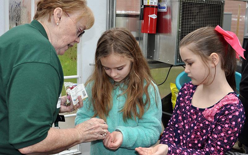 Master Gardener Denise Atkins, left, carefully places a few seeds in the hands of East Fannin Elementary students Mallory Cline, center, and Cora Burnette during a special class Monday, March 3.