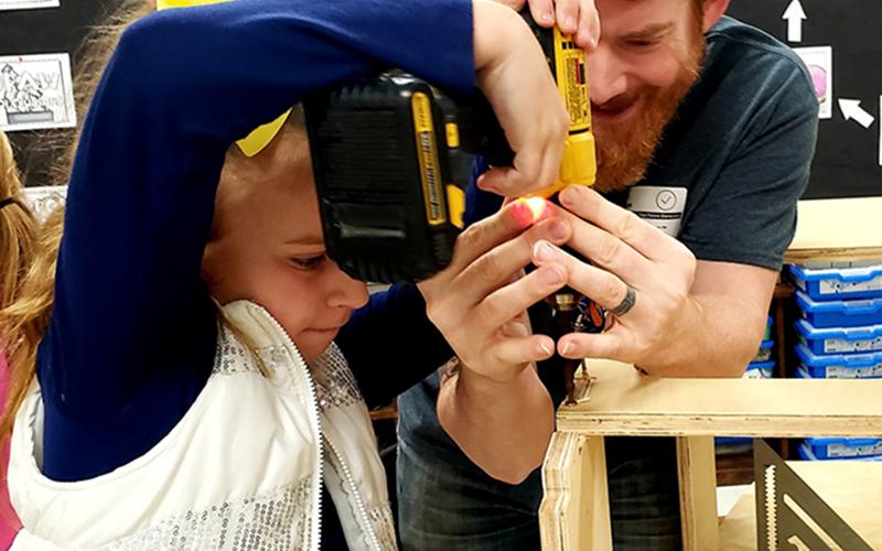 East Fannin student Vera Grace Price concentrates as she drills a hole for a racer that will be entered in the Blue Ridge Soap Box Derby. Helping her is event organizer Mike Sullivan.