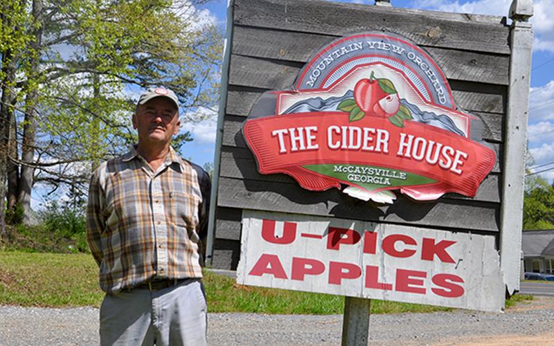 Mountain View Orchards Founder Joe Dickey stands beside a sign carrying a logo for the former restaurant.