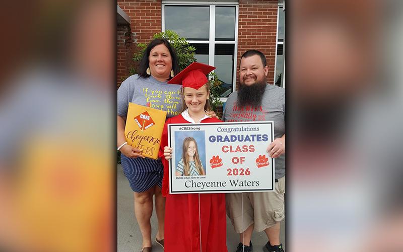 CBES graduate Cheyenne Waters smiles as she shows off her sign with teachers Jennifer Speights and Andrew Cook.
