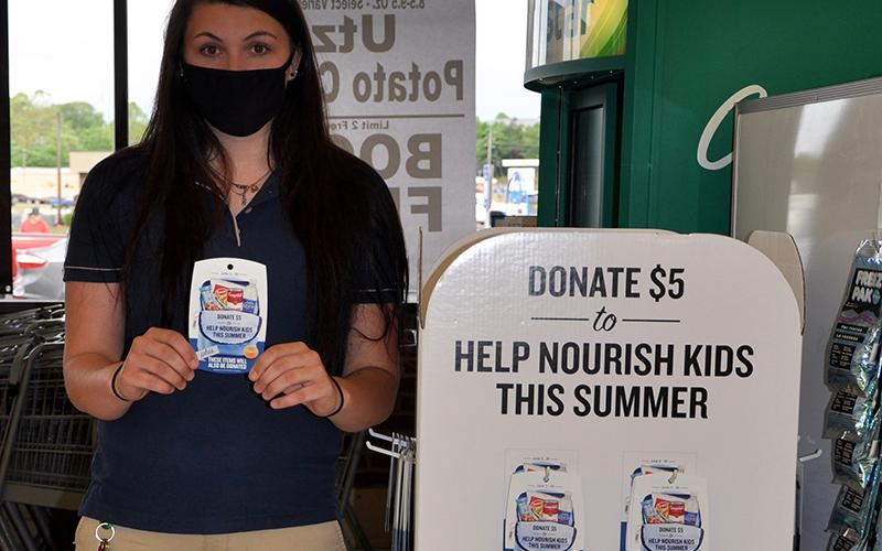 Blue Ridge’s Food Lion Customer Service Lead Helen Ramey holds up a hang tag for customers to grab if they want to contribute to Summers Without Hunger. Next to her is a display, right next to their CoinStar machine, where the tags may be found.