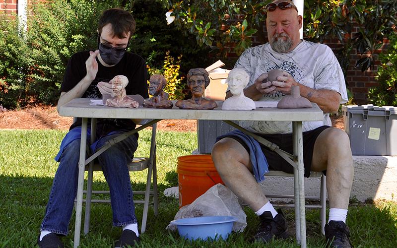 Fine Art Potters, left, Devin Weeks and Mike Lalone sculpt out some figures outside of the Crossroads: Change in Rural America exhibition at The Art Center Saturday, June 20.