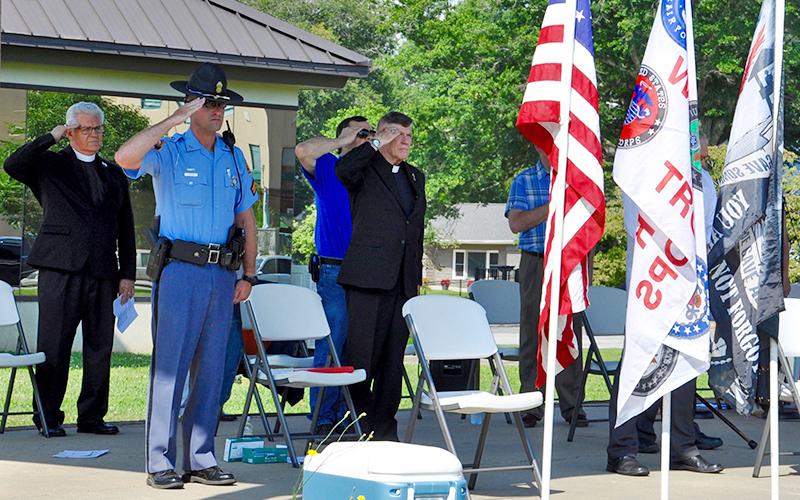 Local clergy members, law enforcement officers, first responders and community members gathered in Blue Ridge’s downtown park to pray for the nation Saturday, July 18. Public servants are shown saluting the flags during the National Anthem.