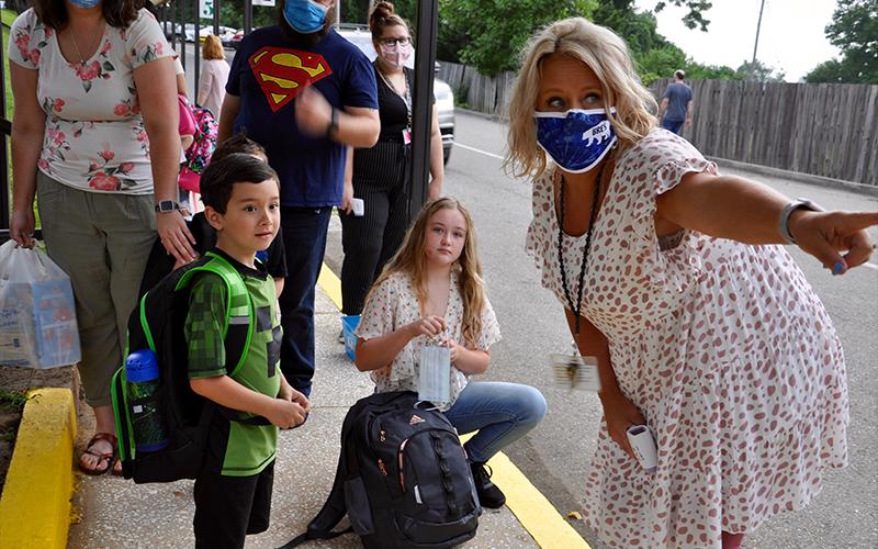 Technology Specialist Brandi Holloway points Layne Pope in the right direction on the first day of school. Jaelyn Breaus gets out her mask in the background.