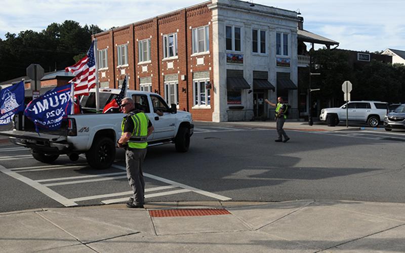 Blue Ridge police officers, from left, Patrolman Thomas Davis, Captain Robbie Stuart and Chief Johnny Scearce, are shown directing one of the approximate 50 to 75 vehicles flying a variety of flags through Blue Ridge Saturday evening. They are at the intersection of West Main and Depot streets.