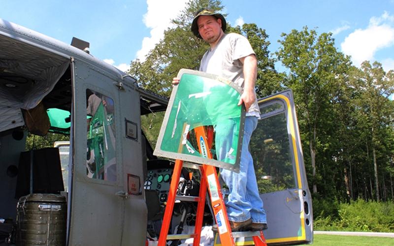 Fannin County Veterans Museum Curator Trevor McIntyre is shown holding up the damaged greenhouse window of the Huey.
