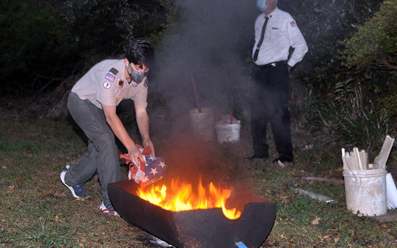 Boyscout Chase Roll gently lays a retired flag into the fire to be burned at a Flag Retirement Ceremony at Horseshoe Bend Park Tuesday, October 20.