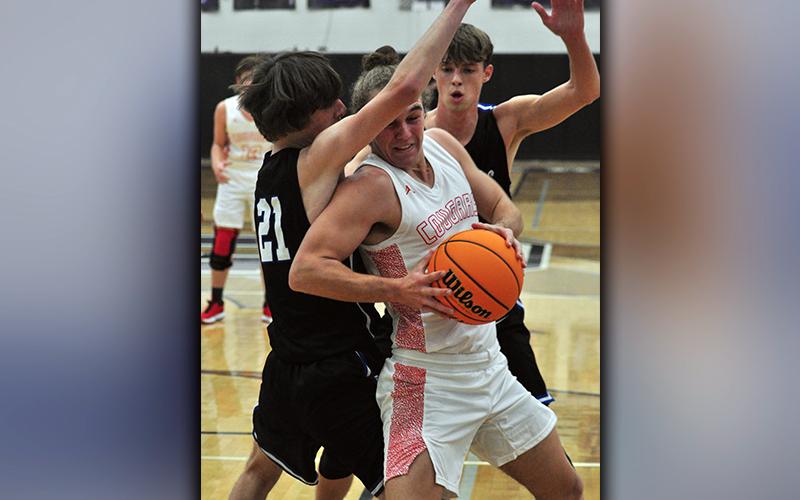 Cougar Radford Cheek (11) muscles through Rebels Nick Arp (21) and Kaeden Twiggs (5) during the Rebels and Cougars basketball game Tuesday, November 24.