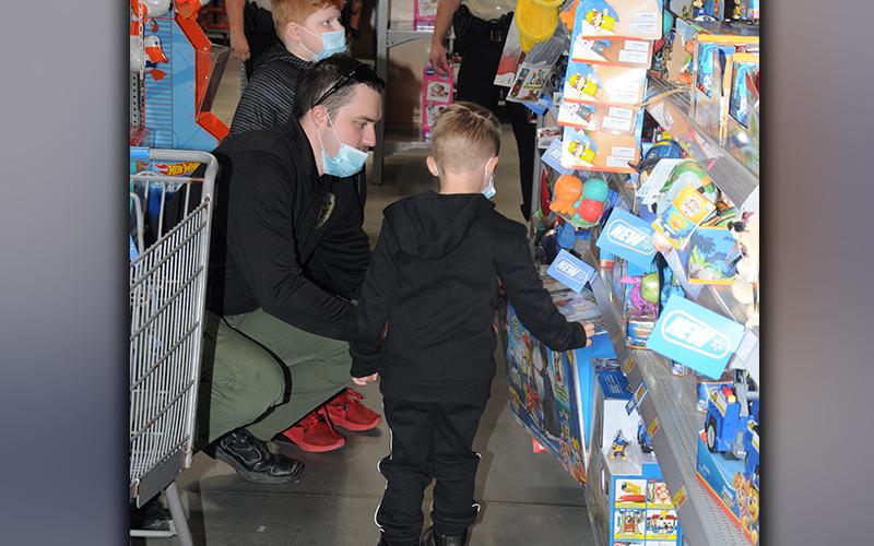 Fannin County Detention Sergeant Tyler Limburg had his hands full helping two youngsters pick out gifts during Shop With A Cop Saturday.