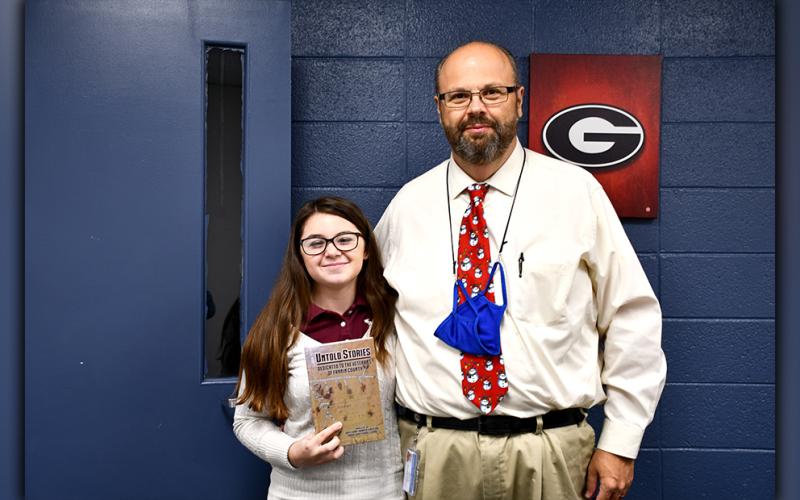 Fannin County High School student Emma Pittman and Fannin County Middle School Assistant Principal Mark Young display the Untold Stories book produced at the middle school by the Ignite Grant Board of Directors and dedicated to the veterans of Fannin County.
