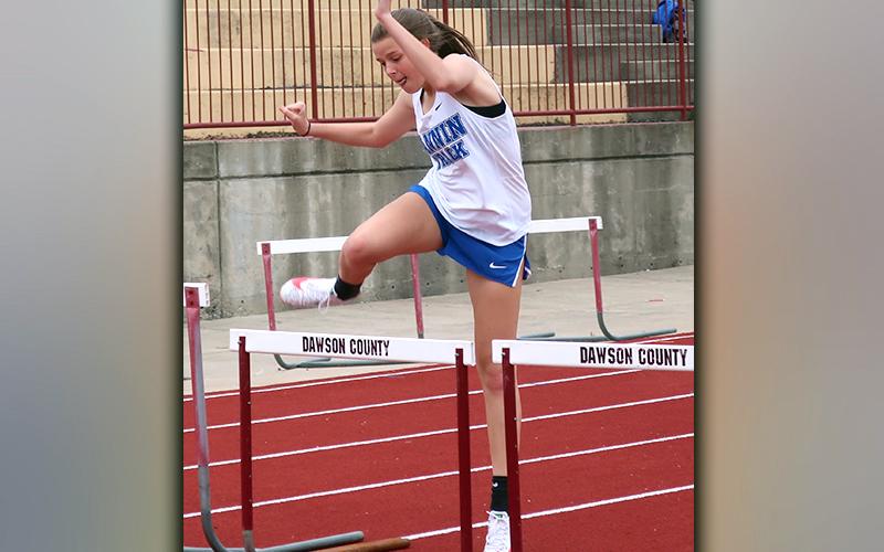 Lady Rebel Macy Hawkins jumps over a hurdle in the 200 meter event at the Dawson County tri-meet between the Rebels, Tigers and Johnson High School. Hawkins placed second in the event and finished with a time of 26.91.