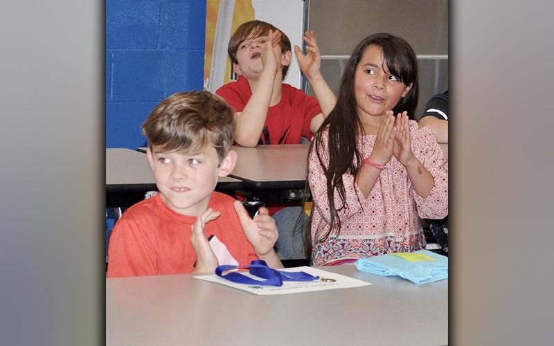 East Fannin Elementary School students, from left, Adam King, Waylon Williams and Liliana Ruiz clap for their peers as the 4-H Project Achievement Awards were announced.