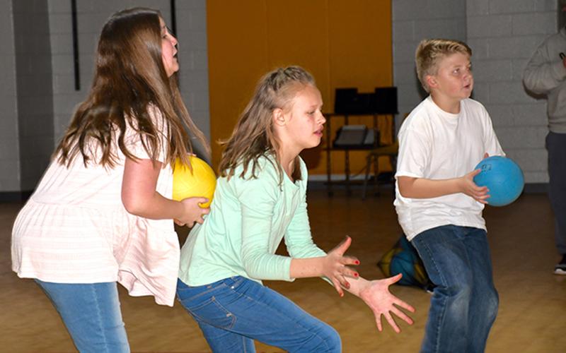 West Fannin Elementary School students Addison Graham, Kaylee Dyer and Brody Graham, shown from left, prepare to select the correct answer to a math problem by throwing a ball at their answer choice on the Lu Interactive Playground screen Tuesday, March 2.