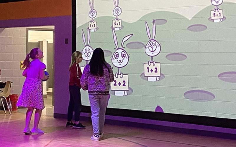 West Fannin Elementary School students are now able to continue learning new academic lessons outside of the classroom thanks to the gym’s new Lu Interactive Playground. Students are shown, above, excitedly answering math problems in a gym that has been transformed with technicolor lights and an interactive screen.