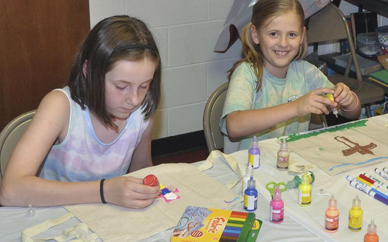 Bailey Abbot, left, and Kristi Holland decorate their Bible cases during arts and crafts at Pleasant Hill Baptist Church’s VBS Wednesday, June 9.
