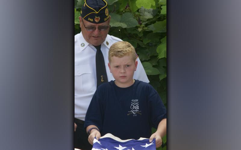 Blue Ridge Elementary School fifth grade student Owen Norton folds an American Flag properly while North Georgia Honor Guard member Richard Crosley instructs from behind.