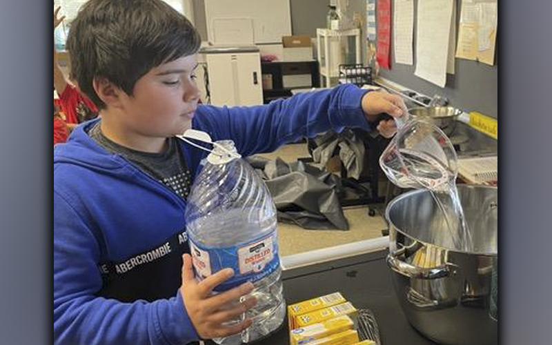 Grayson Woody adds water to the gelatin mixture in order to make pineapple flan as part of a lesson with fourth-grade students at West Fannin Elementary School that tied in several school subjects.