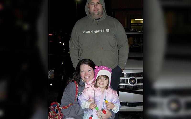 Kim holding Kaylynn, and Jeremy watch from Mountain Street as the Blue Ridge Business Association Light Up Blue Ridge Parade passes.