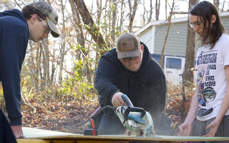 Fannin County High School students Trey Combs, Brandon Rhodes and Paul McCormick, from left, work together to saw a piece of plywood for the latest Habitat for Humanity of Fannin &amp; Gilmer Counties build Friday, December 3.