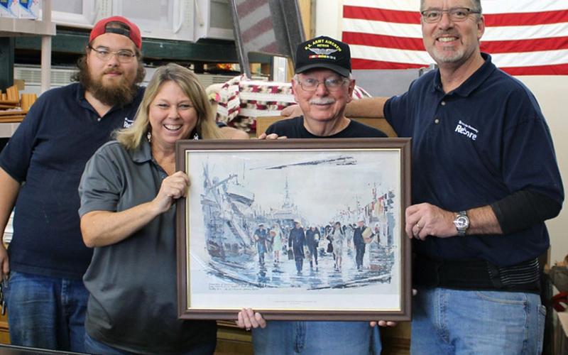 Habitat for Humanity of Fannin &amp; Gilmer Counties’ ReStore Manager Jeanett McTaggart  hands off a World War II unit painting to veteran Rod McIntyre with the Fannin County Veterans Museum. Around them are, from left, Ryan Maston and Salvatore Maniscalco.