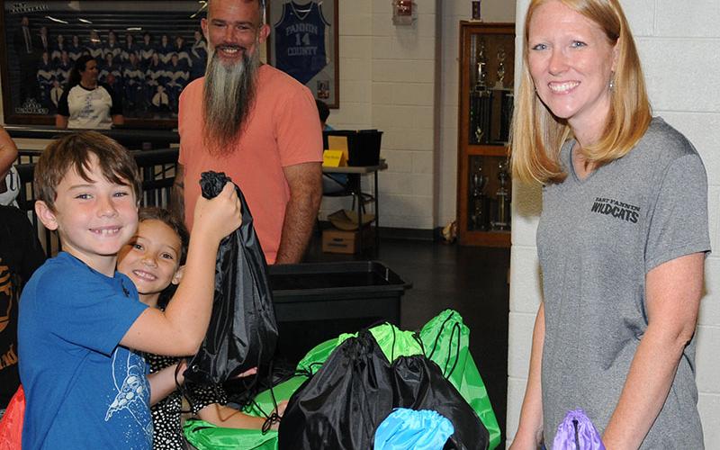 Myles shows off his bag of school supplies while Ellie, in the background, enjoys the moment. Sylas was close by. The supplies were being passed out by Amanda McBride, right.