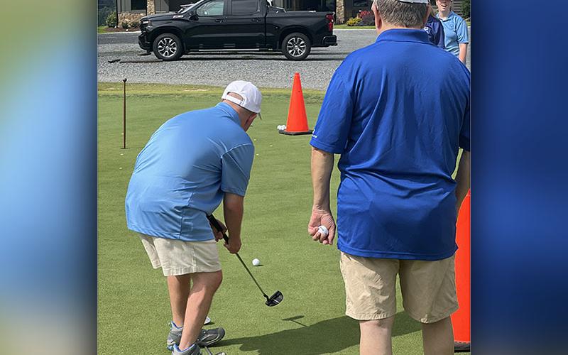 Jay Jenkins, left, takes a putt towards the hole with the guidance of Tom Neuman, right, at the Special Olympics golf event Tuesday, July 19 at Old Toccoa Farms.