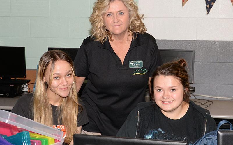 Mountain Education Charter High School (MECHS) Principal Vicky Henry, standing, is shown helping Twyla Benefield (left) and Mattie Coffee during a class at the Blue Ridge campus.