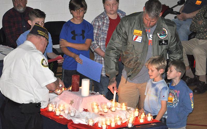 West Fannin Elementary School students, from left, Bently Cole, Colton Dills and Jonah Strobel watch as Joey Gryzenia, a member of the US Coast Guard, participates in the candle lighting ceremony at their Veteran’s Day Progam. To his right are his sons Maddox Gryzenia and Miller Gryzenia who are also students at West Fannin.
