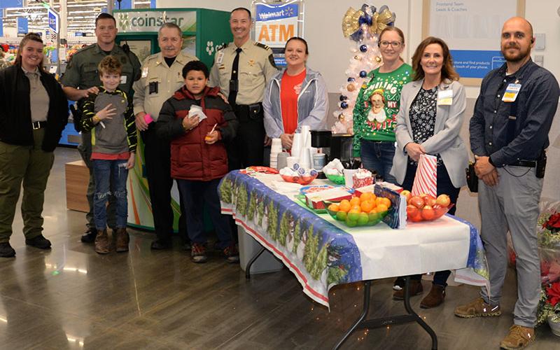 At the end of their shopping trip at Walmart in Blue Ridge, children were treated to hot chocolate, cookies, candy and fruit. Shown as two youngsters find plenty of treats are, standing from left, detention officer Kacy Godsey, Department of Natural Resources K-9 officer Jared Woods, Deputy Cecil Davis, Lieutenant Darvin Couch, Shop With a Cop board member Dawn Cochran, Elizabeth Hutsell of Walmart, Walmart Manager Sherry Neal, and Cameron Miller of Walmart. .