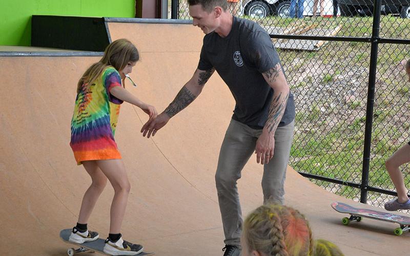 Austin Leach, director of Highland Outdoor Ministry, works with a young skater as she learns how to ride a skate board at Syd’s Place.