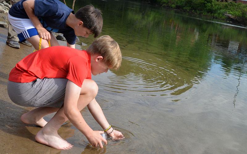 Kendrick Pack, foreground,  and Alex Barber are careful to make sure the small rainbow trout they raised in their Fannin County Middle School classroom are safely released into the Toccoa River.