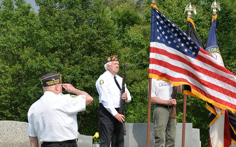 Gerald “Chief Mac” McMillian salutes as Ron Wallace and other members of the North Georgia Honor Guard prepare for a rifle salute at Crestlawn Cemetery.