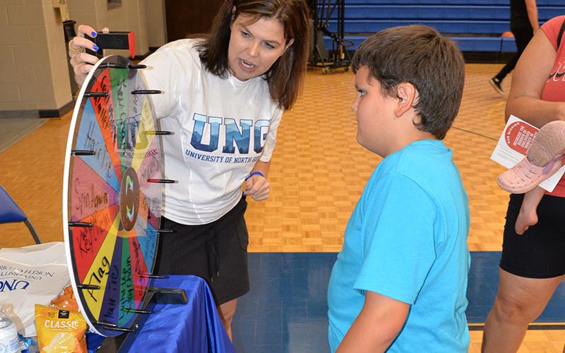 Deb Cantrell of the University of North Georgia Blue Ridge campus helps a young man take a turn on the school’s prize wheel at Saturday’s bash.