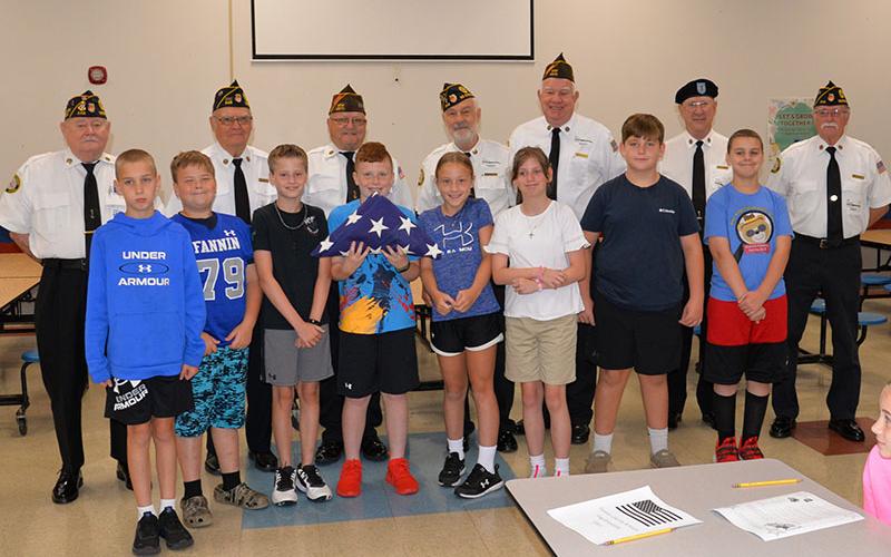 Blue Ridge Elementary School fifth grade students from left, front, Justin Burrell, Mason Patterson, Aiden Owensby, Zeke Payne, Alexandria Evans, Annabelle Rainwater, Cason Dyer, and Troy Taylor display the American flag that they just practiced folding as veterans Chief “Mac” McMillen, Chris McKee, Richard Crosley, Steve Strickland, Jim Wallace, Bob Herrington, and Bill Stodghill stand behind them.
