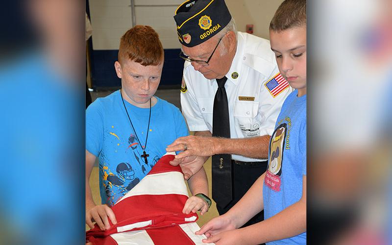 Blue Ridge Elementary School fifth grade students Zeke Payne and Troy Taylor follow instructions from veteran Chris McKee as he demonstrates how to tuck the folds of the United States flag neatly. This was part of a local program offered by area veterans organizations.