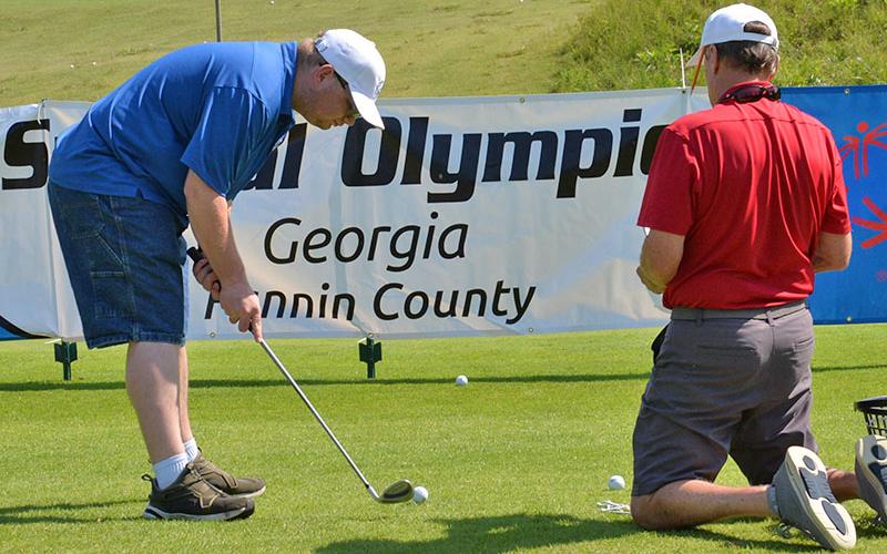 Taylor Carroll lines up a chip shot, which must go over the Special Olympics banner, as coach Craig Hartman keeps a close eye on the golfer’s expertise.