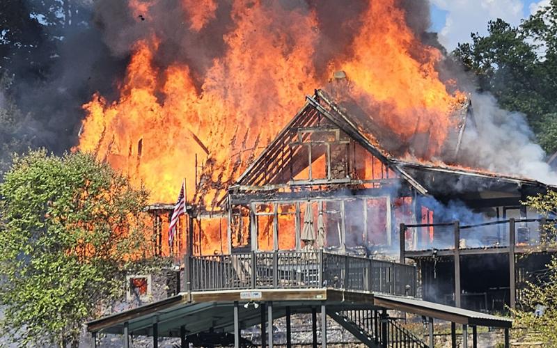 This photo of a fire at a Blue Ridge Lake home was believed to have been taken only minutes after firefighters were called to the scene shortly before 3 p.m. last Wednesday, July 26. The resident who was at home reported discovering the blaze when the entire front of the structure, facing the lake, was already fully involved in flames. Neighbors removed the boat shown in the foreground to a different dock.