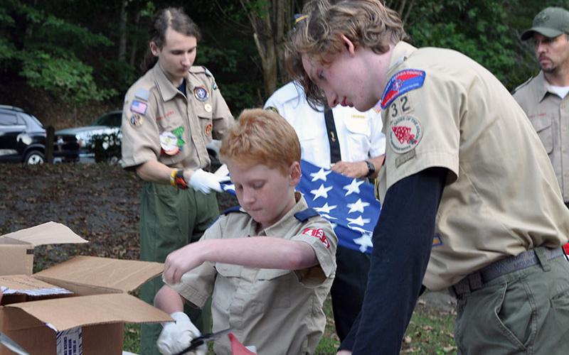 Mathew Monroe of Boy Scout Troop 32 helps a young Cub Scout, Ethan Threet, during the ceremony at Ron Henry Horseshoe Bend Park last Tuesday evening. They are working together to inspect and cut a flag separating the canton from the stripes so it can be retired properly.