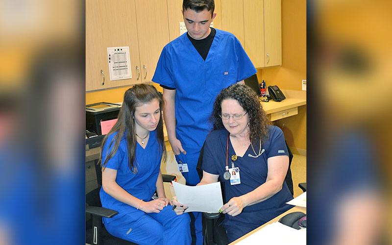 Students Blair Deal and Trent Davis look over a patient’s chart with LPN Candy Burgess at Georgia Mountains Health. The two students are juniors at Fannin County High School and are a part of the General Medicine class’ clinical rotation program.