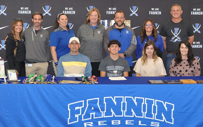 Proud coaches and volunteers pose with Zechariah Prater, seated with his family, when he signed his Letter of Intent to run track and field at Charleston Southern University. Shown from left are Head Coach Miranda Roof, volunteer coach Dr. Lucas Roof, Hannah Godfrey, Suzianne Pass, Principal Scott Ramsey, Athletic Director Shannon York, and volunteer coach Chad Galloway.